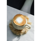 Tasse en céramique crème avec latte art sur sous-verre rond en raphia frangé