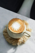 Tasse en céramique crème avec latte art sur sous-verre rond en raphia frangé