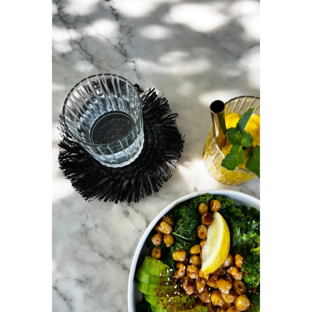 Saladier vert avec avocat, pois chiches rôtis et tranche de citron, dessous de verre rond en raphia noir avec franges