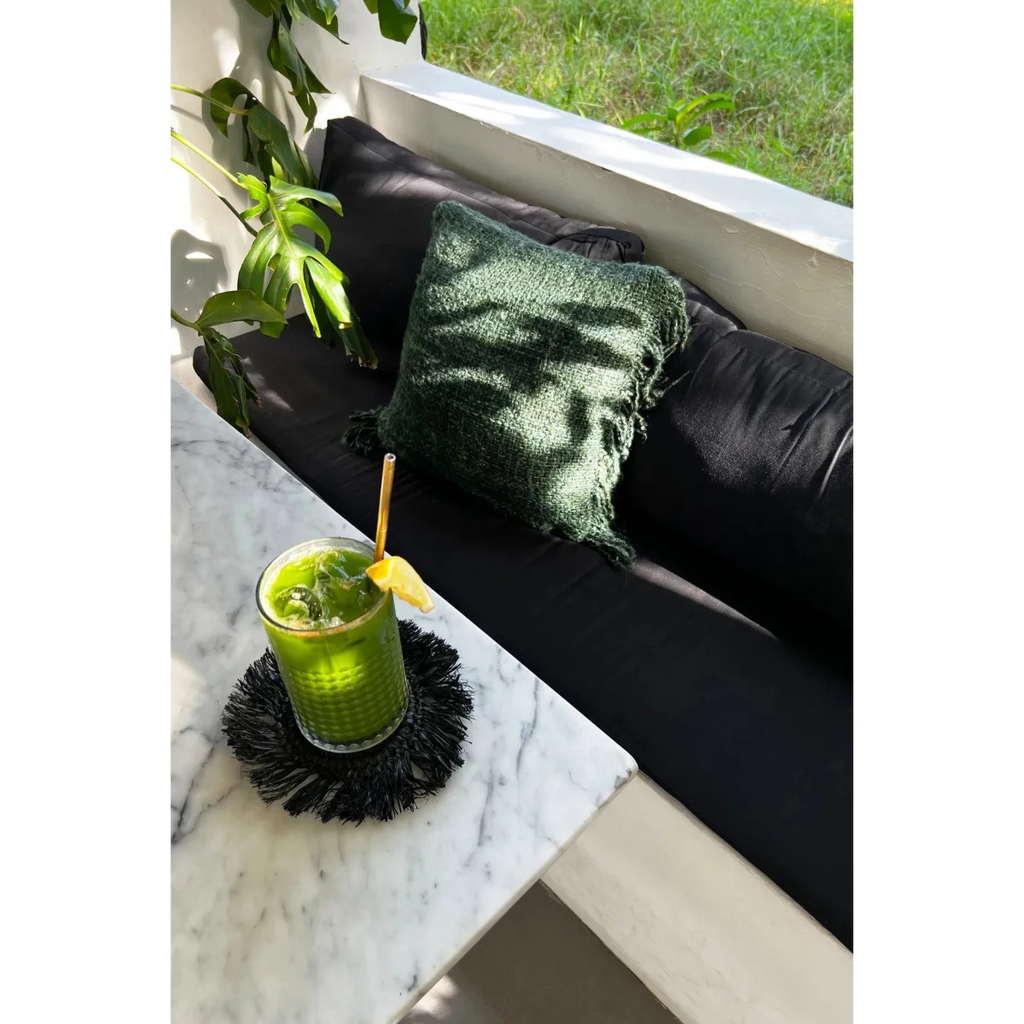 Smoothie vert dans un verre avec paille en or et tranche de citron, sur un dessous de verre rond en raphia noir avec franges