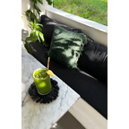 Smoothie vert dans un verre avec paille en or et tranche de citron, sur un dessous de verre rond en raphia noir avec franges