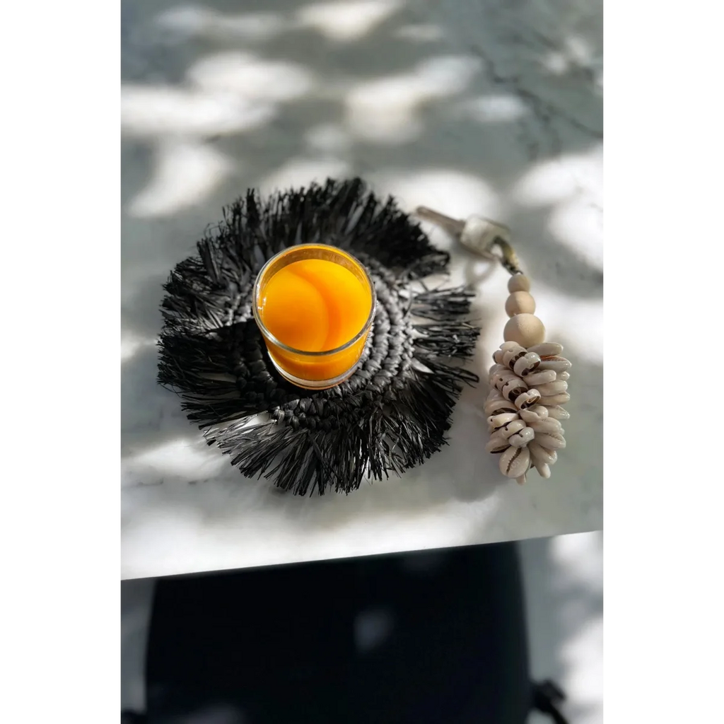 Verre de jus d’orange sur un dessous de verre rond en raphia noir avec franges