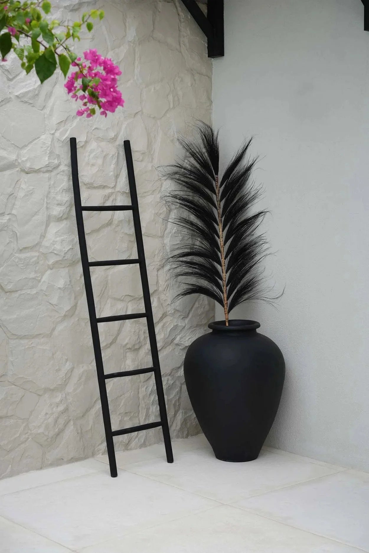 Échelle décorative en teck noir de 165 cm contre un mur en pierre blanche