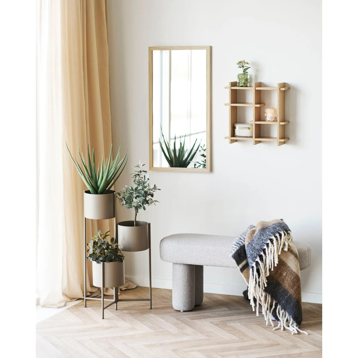 Banquette gris clair avec jambes cylindriques et couverture à franges sur une étagère murale en bois