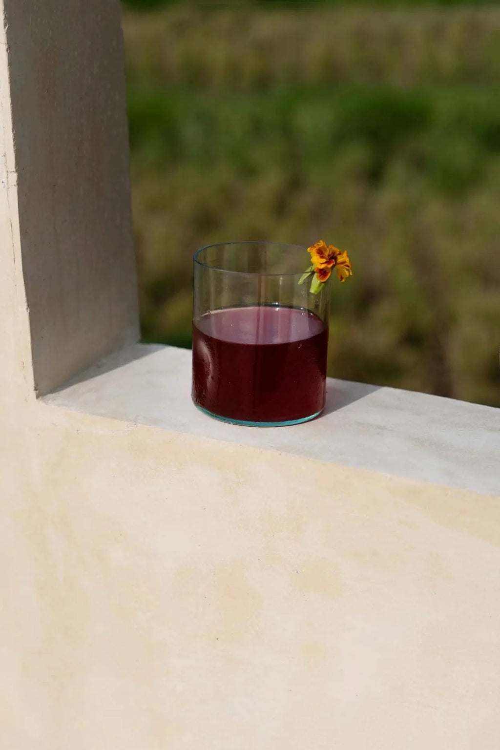 Gobelet en verre recyclé vert organique rempli de liquide rouge et fleur orange