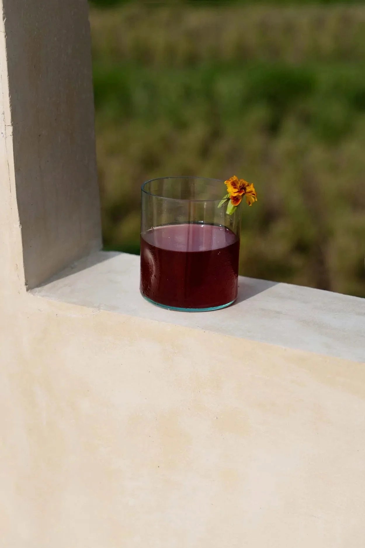 Gobelet en verre recyclé vert organique rempli de liquide rouge et fleur orange