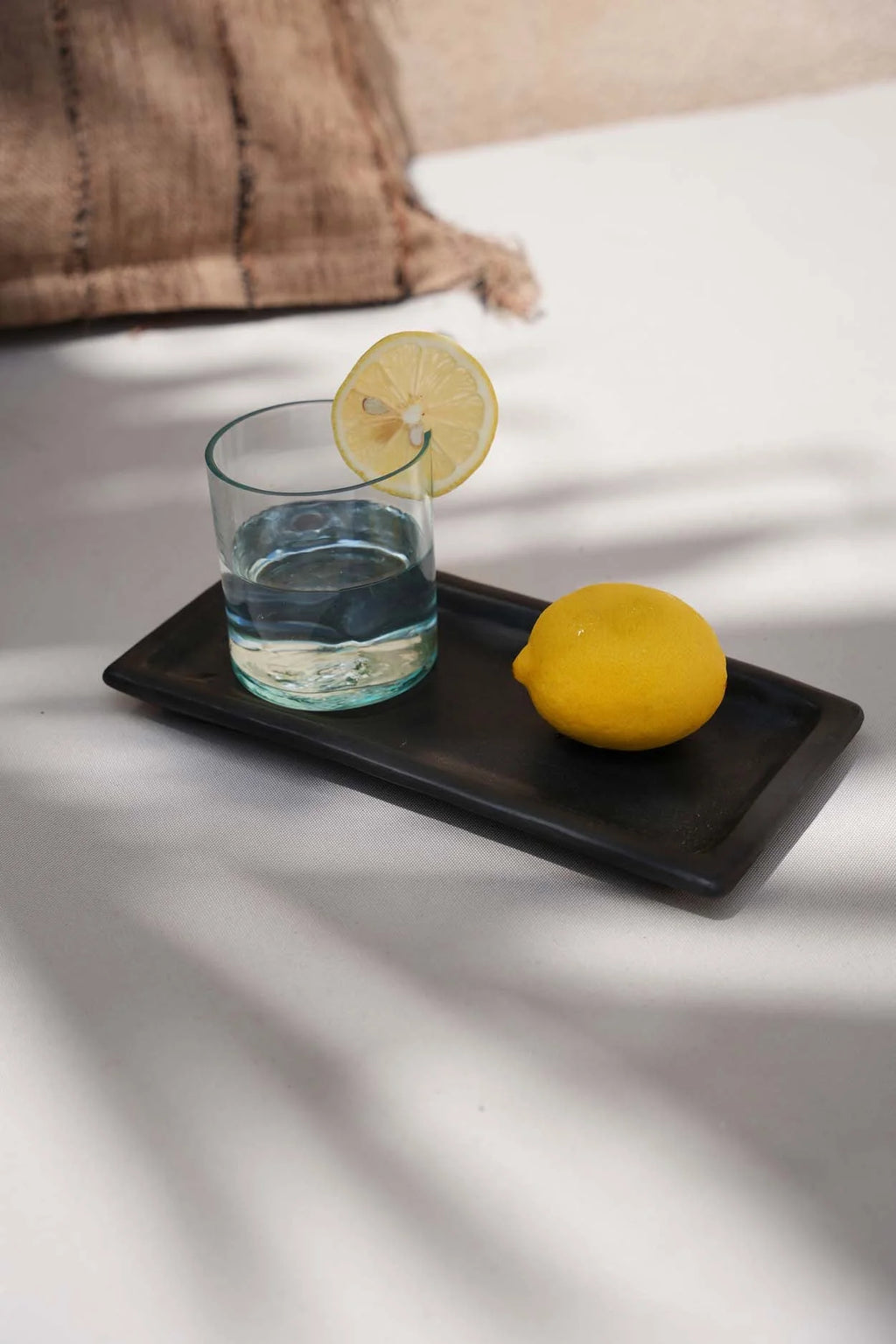 Plateau rectangulaire foncé avec gobelet verre recyclé vert d’eau organique, eau citronnée et citron jaune