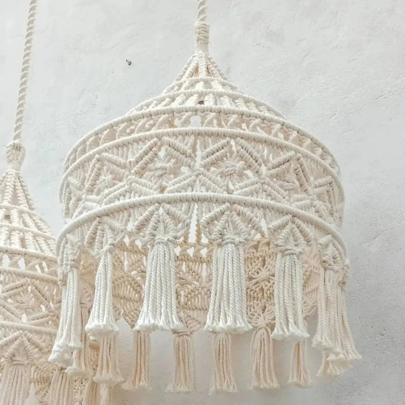 Deux abat-jours en macramé suspendus côte à côte, affichant un style bohème chic avec des franges longues et des motifs tressés.