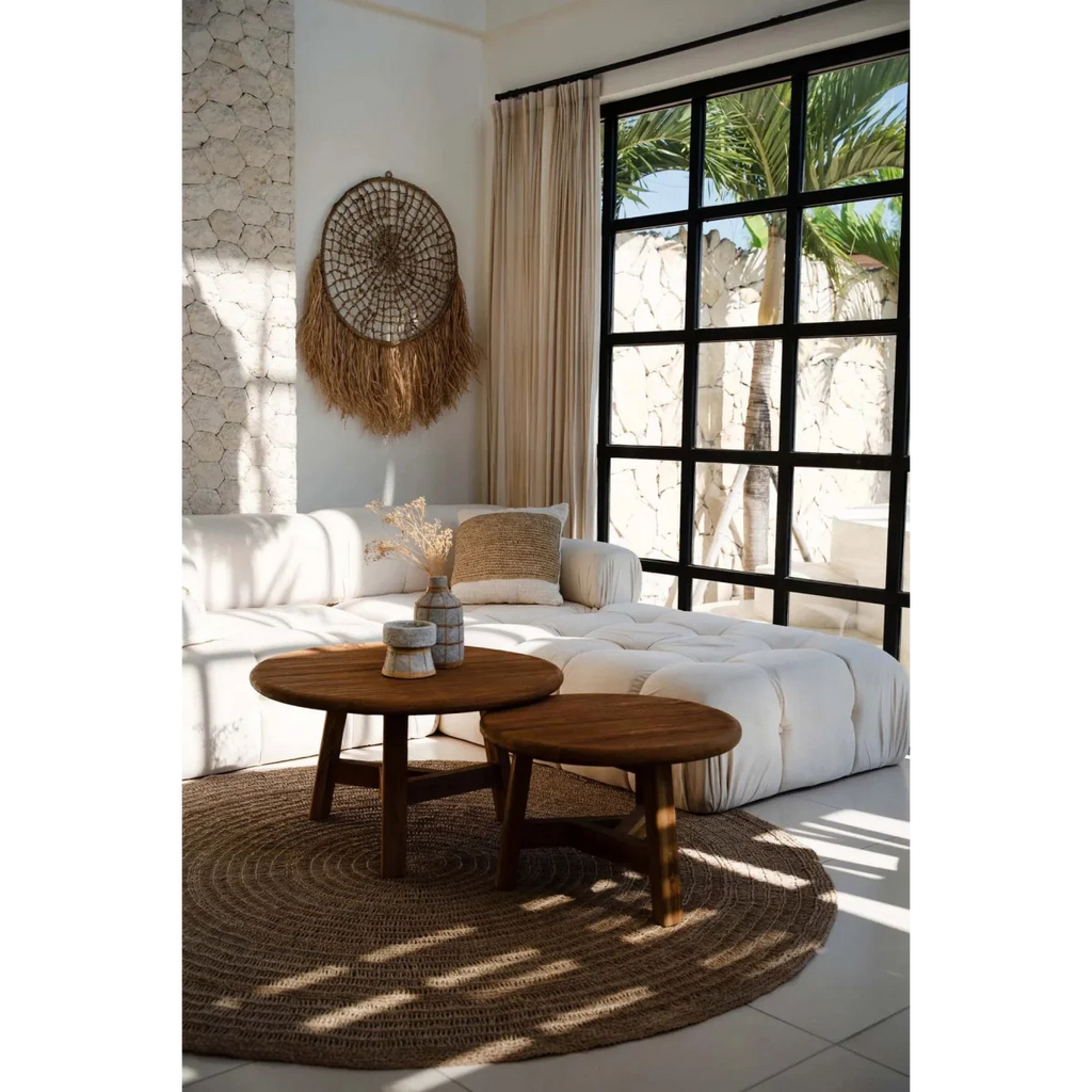 Salon cosy avec sofa blanc, tables rondes en bois et vue tropicale, mural rond en raphia
