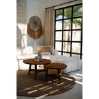 Salon cosy avec sofa blanc, tables rondes en bois et vue tropicale, mural rond en raphia