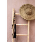 Chapeau paille sombrero avec perles noires et pompon sur échelle boisée contre mur rose