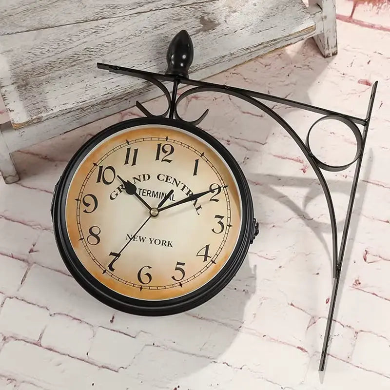 Horloge murale double face vintage posée sur un sol en briques avec support en métal noir
