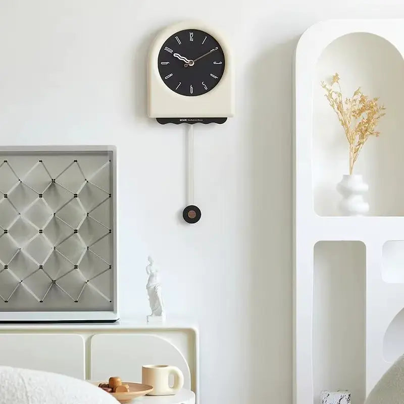 Horloge à pendule moderne crème avec cadran noir installée sur un mur blanc dans un intérieur design et épuré.
