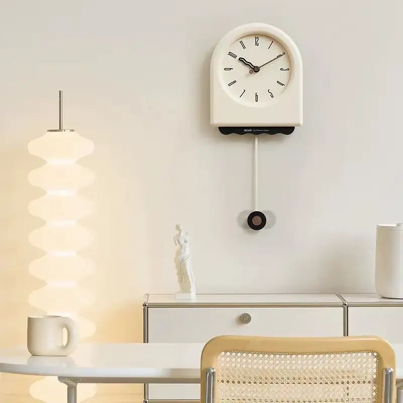 Horloge à pendule moderne crème installée dans un salon au style bohème avec une table en rotin et décoration minimaliste.