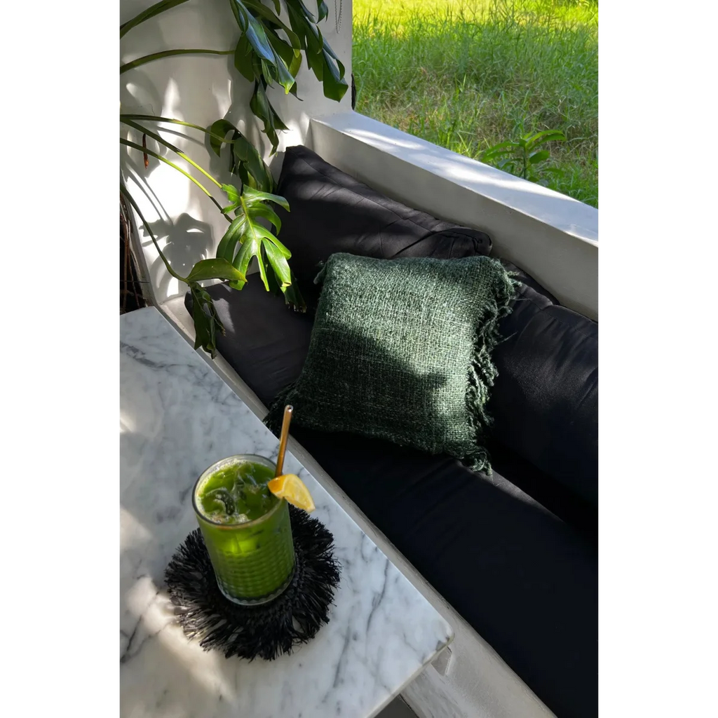 Verre vert vif avec glace, citron, paille dorée sur un dessous de verre à franges