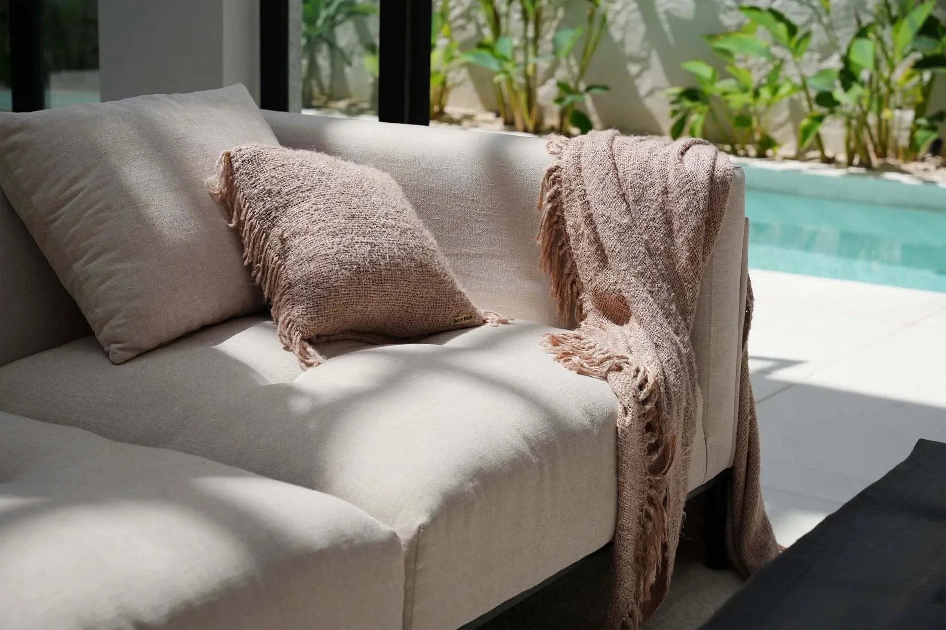 Canapé en lin beige avec coussin texturé et couverture frangée assortie drapée sur l’accoudoir