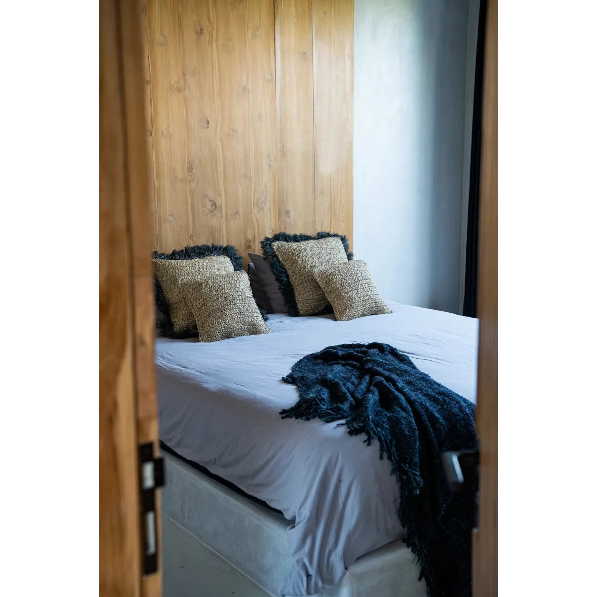 Mur en panneaux de bois avec lit blanc et couverture bleue en raphia tressé