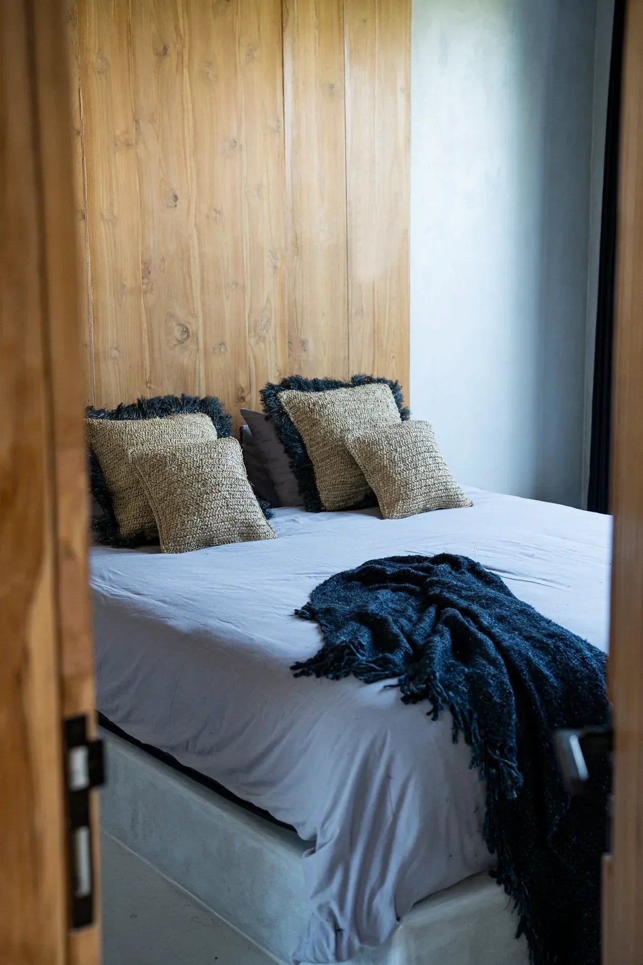 Housse de coussin carrée en raphia naturel tressé sur un lit avec oreillers décoratifs