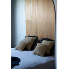 Housse de coussin carrée en raphia noir naturel 60x60 cm sur un lit avec tête de lit en bois