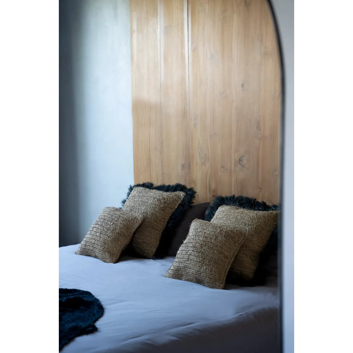 Housse de coussin carrée en raphia noir naturel 60x60 cm sur un lit avec tête de lit en bois