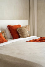 Housse de coussin carrée en velours rouille avec franges sur un lit confortable