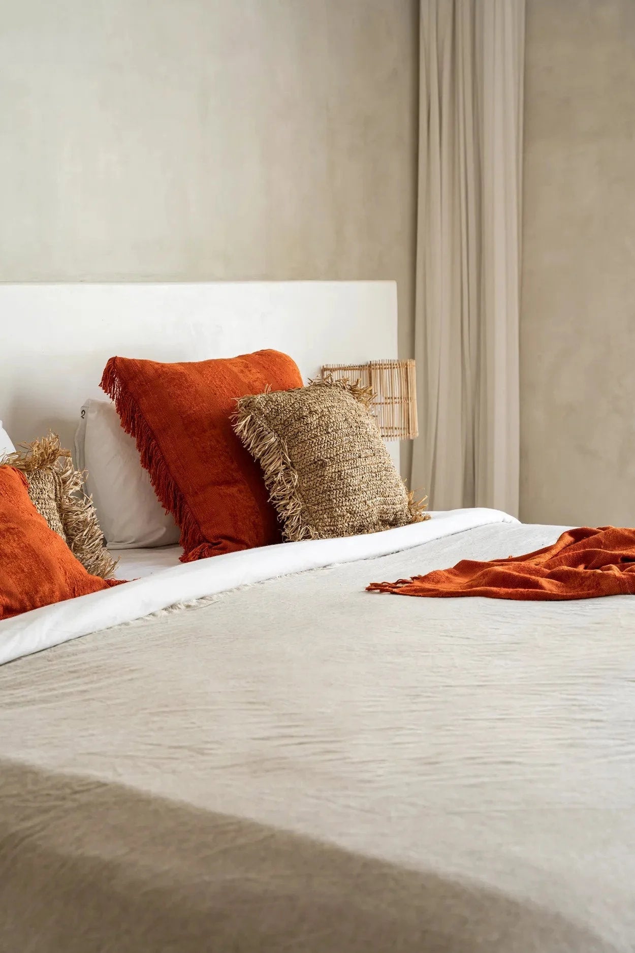 Housse de coussin carrée en velours rouille avec franges sur un lit confortable