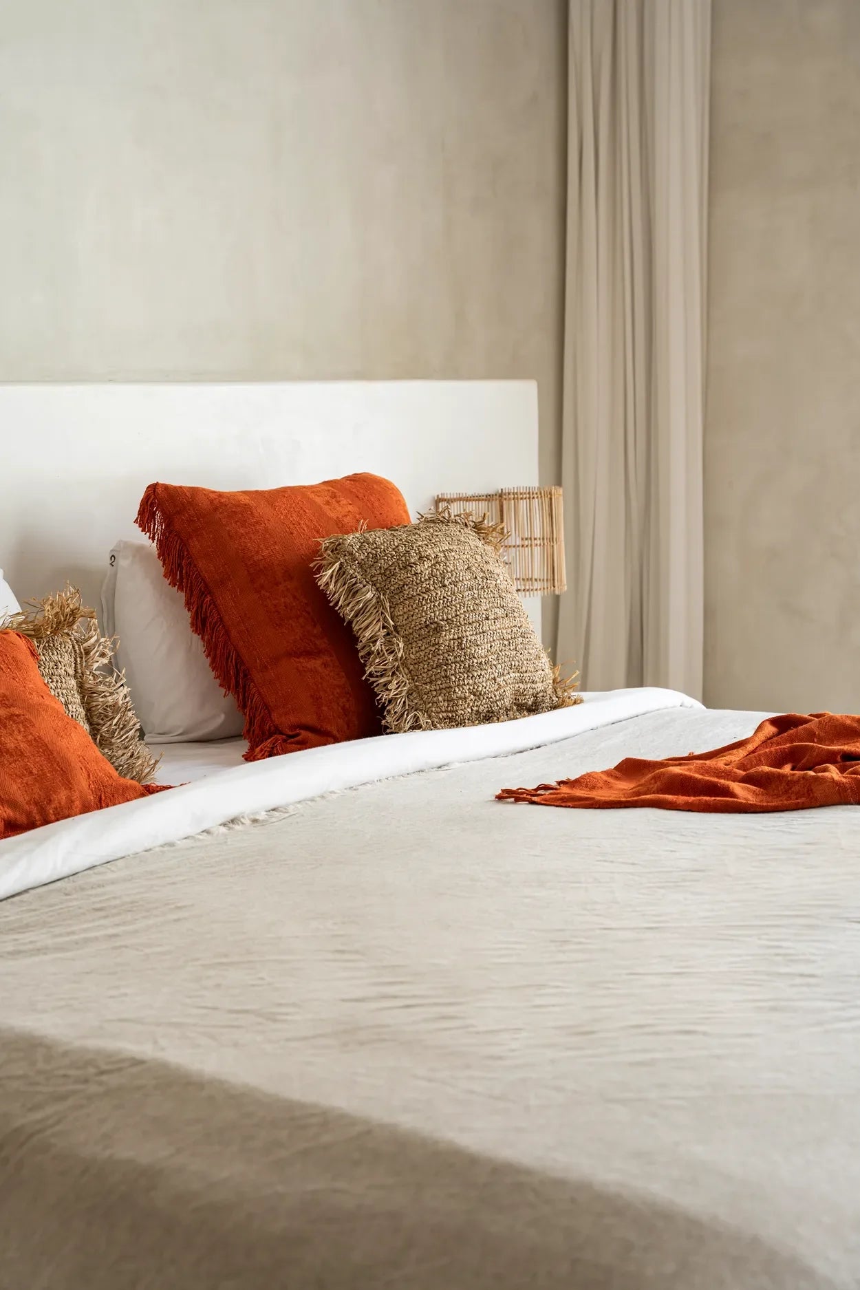 Housse de coussin carrée en velours rouille avec franges sur un lit confortable