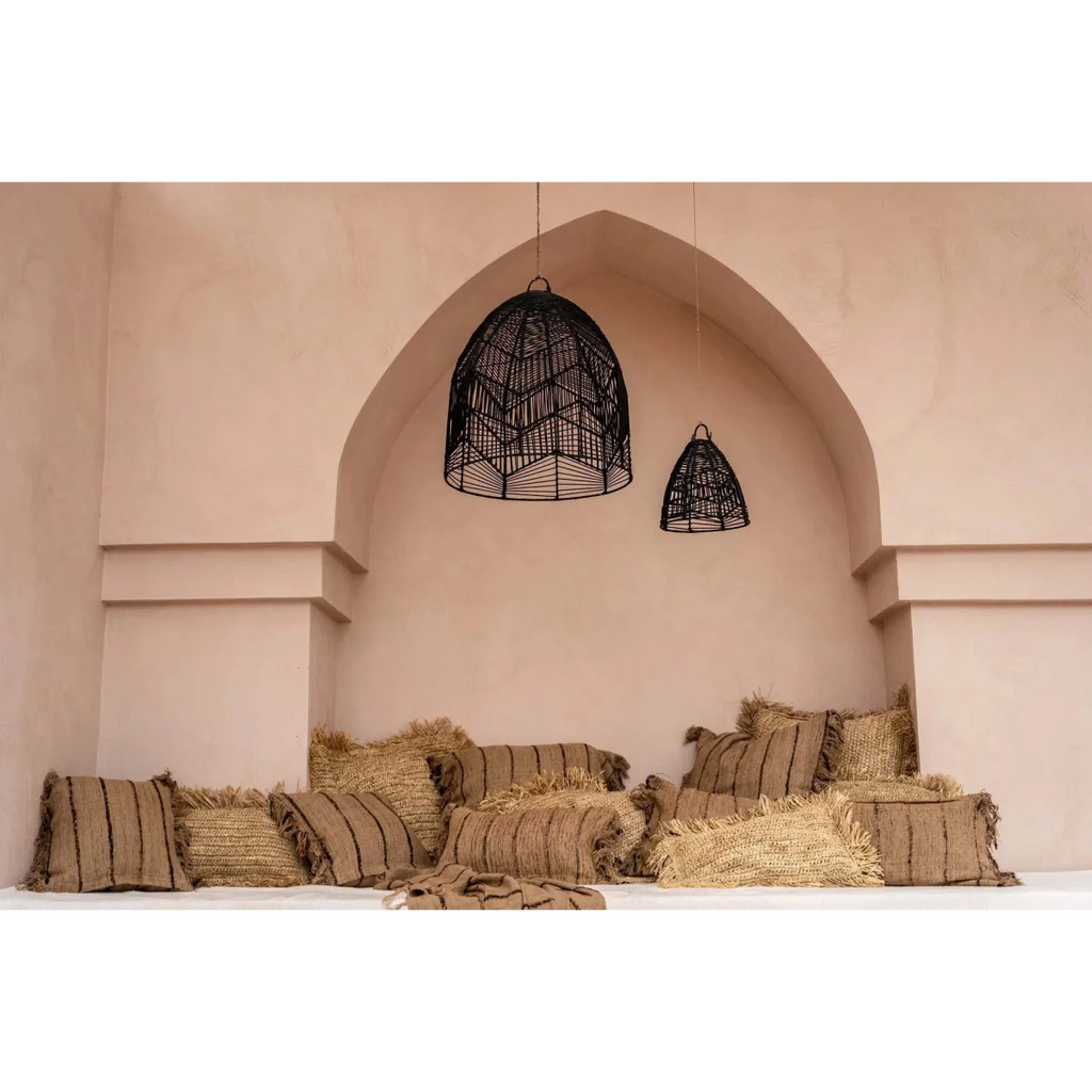 Suspension en osier noir dans une alcôve avec coussins rayés et pailles pour la déco