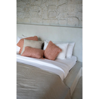 Housse de coussin en coton rose saumon 40x40 cm sur un lit avec draps blancs et coussins beige et coral