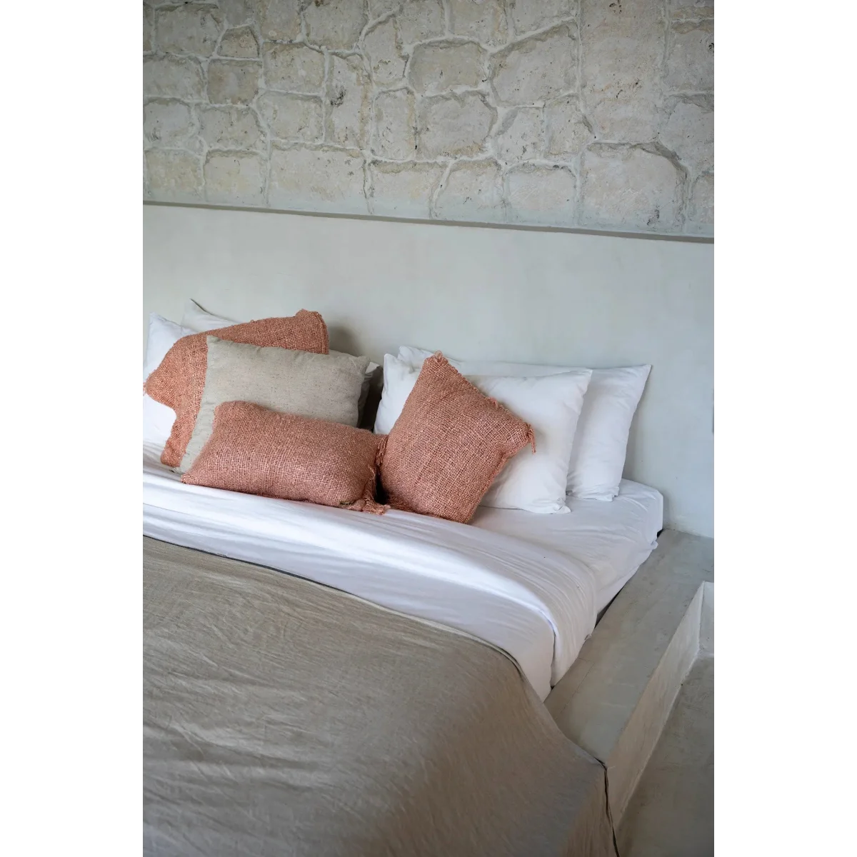 Housse de coussin en coton rose saumon 40x40 cm sur un lit avec draps blancs et coussins beige et coral