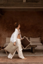 Femme en blanc portant deux coussins : beige texturé et marron à bord crocheté crème