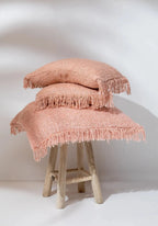 Coussin rectangulaire rose saumon avec franges, textured, sur un tabouret en bois clair