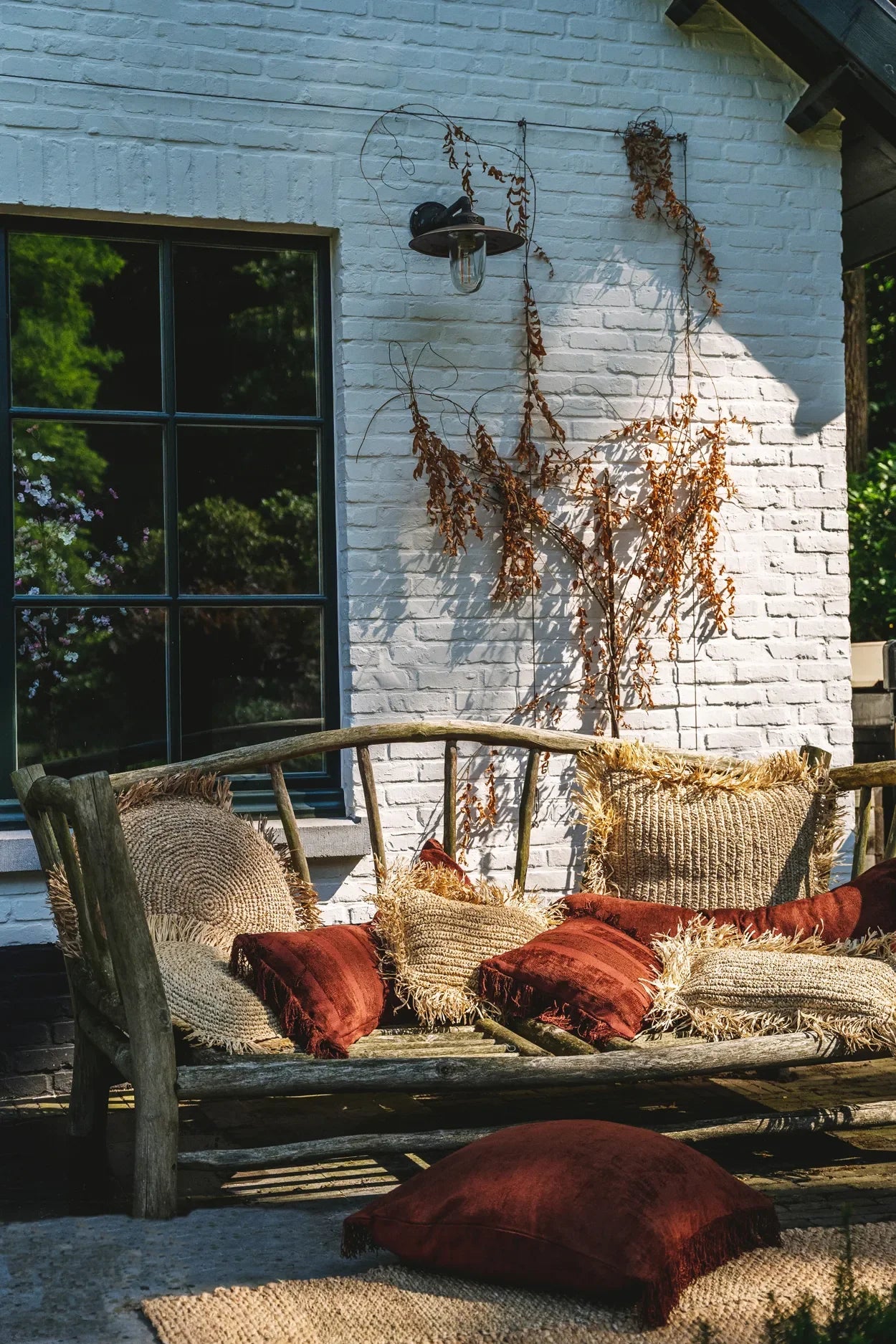 Housse de coussin rectangulaire en velours bordeaux avec franges sur une banquette en bois rustique