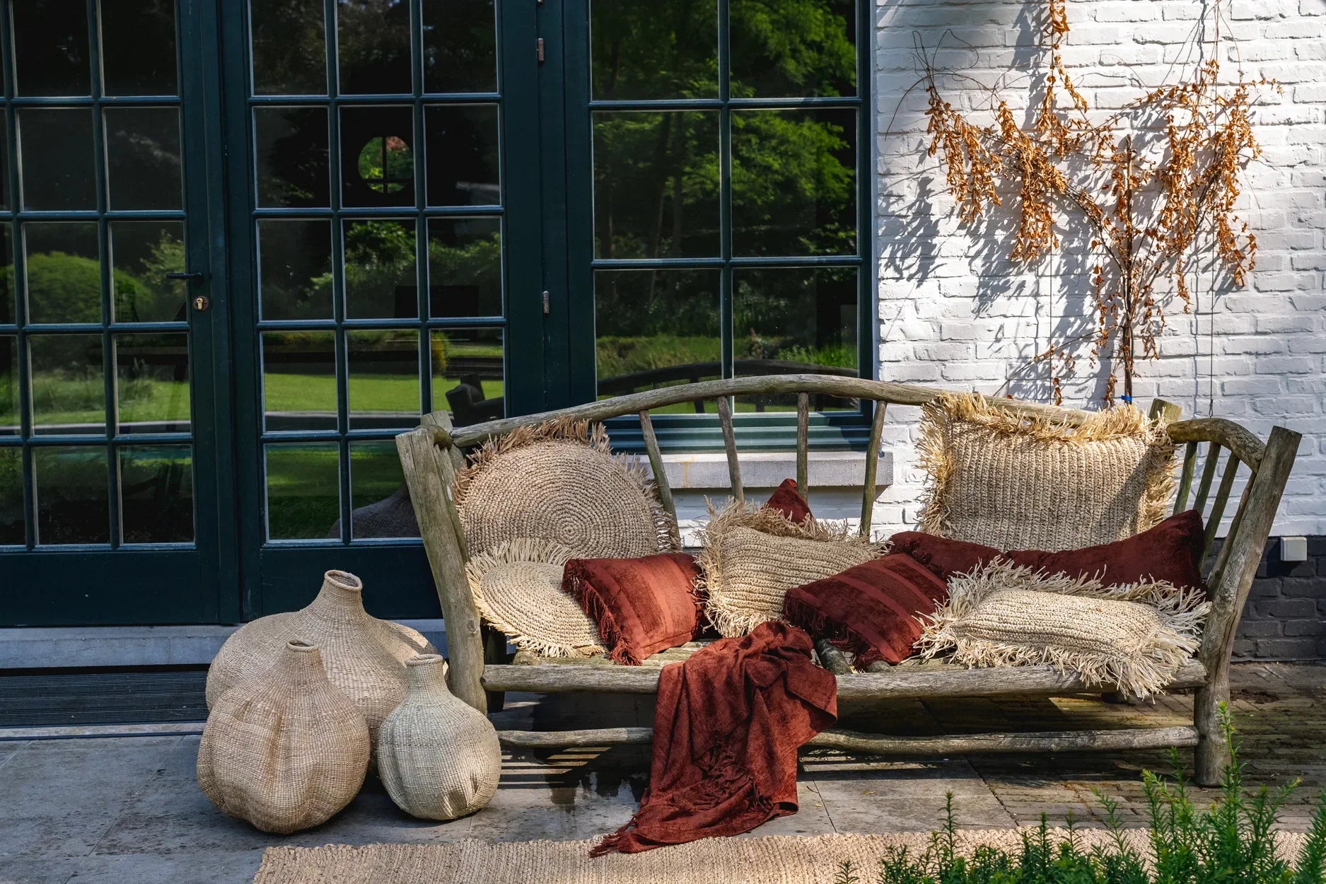Housse de coussin rectangulaire en velours bordeaux avec franges sur un banc en bois rustique