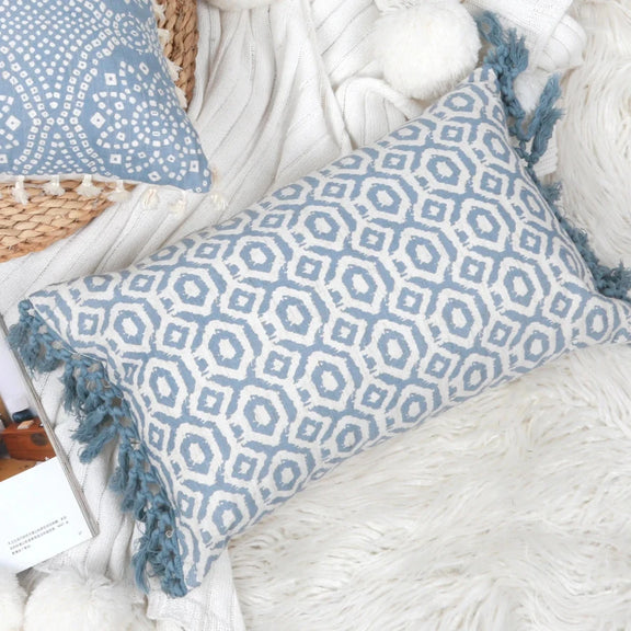 Housse de coussin bleu géométrique avec franges posée sur un canapé