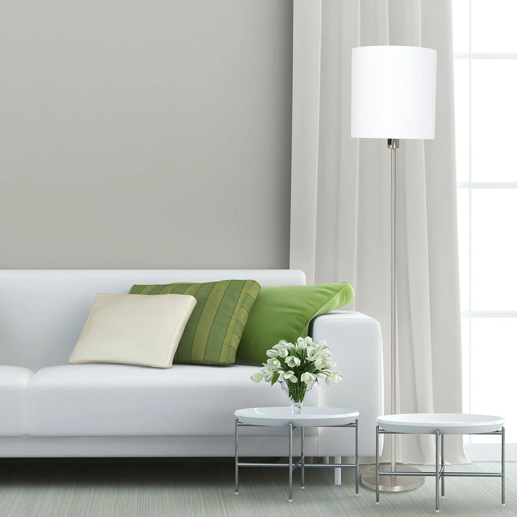 Canapé blanc avec coussins verts et crème dans un salon moderne près d’un Lampadaire en métal brossé