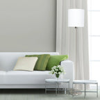 Canapé blanc avec coussins verts et crème dans un salon moderne près d’un Lampadaire en métal brossé