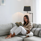 Femme en pull cosy et pantalon blanc lisant sur un canapé avec un petit chien endormi