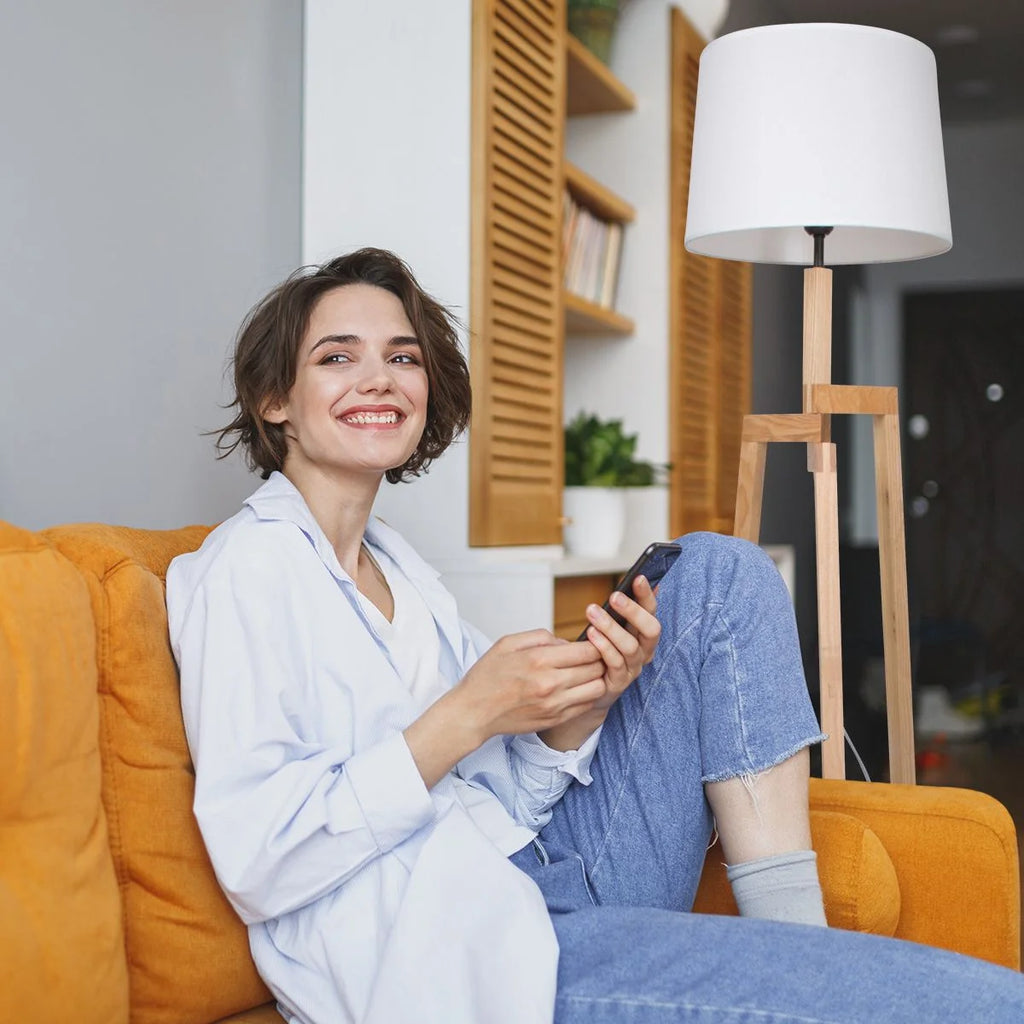 Femme souriante avec cheveux courts portant un jean et une chemise bleue sur un canapé orange