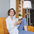 Femme souriante avec cheveux courts portant un jean et une chemise bleue sur un canapé orange