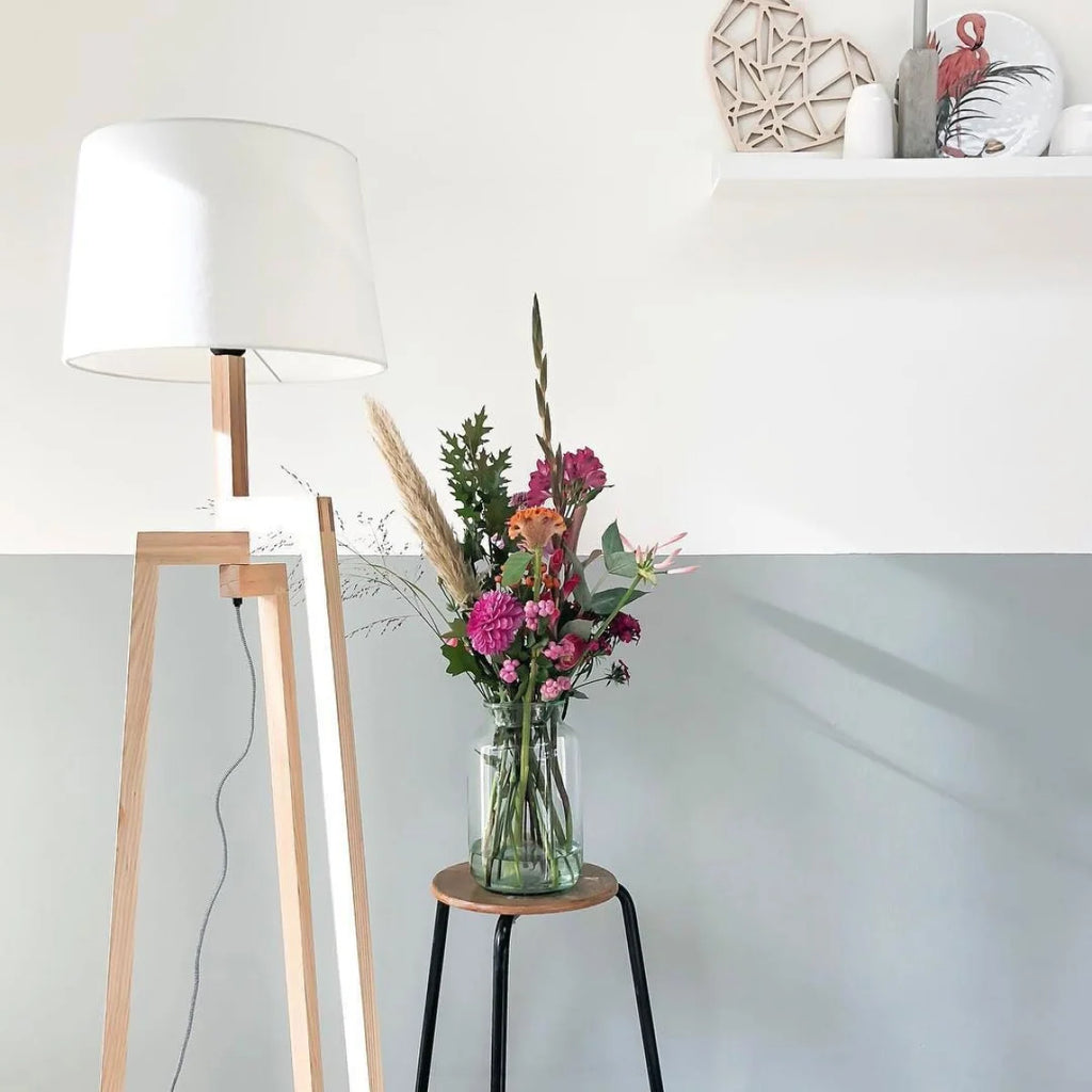 Bouquet de fleurs colorées dans un vase en verre clair avec lampadaire tripode bois