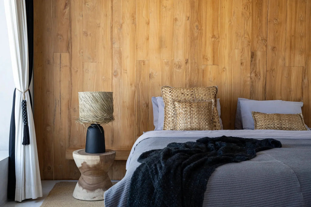 Lampe à poser cylindrique en paille tressée noir et naturel dans une chambre cosy avec mur en bois