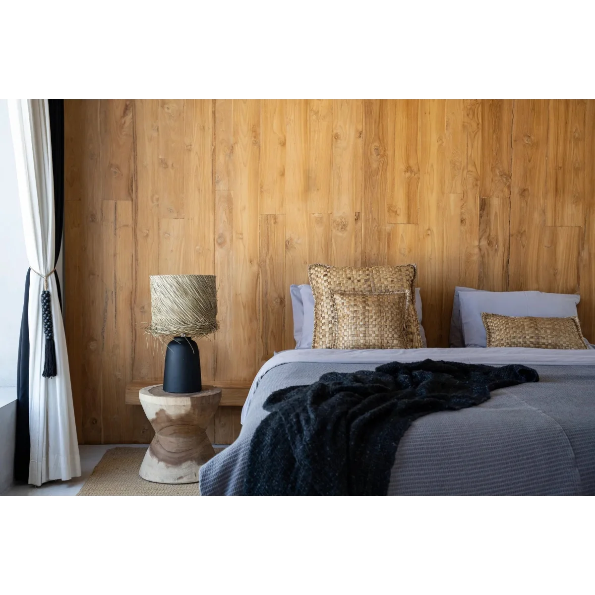 Lampe à poser cylindrique en paille tressée noir et naturel dans une chambre cosy avec mur en bois