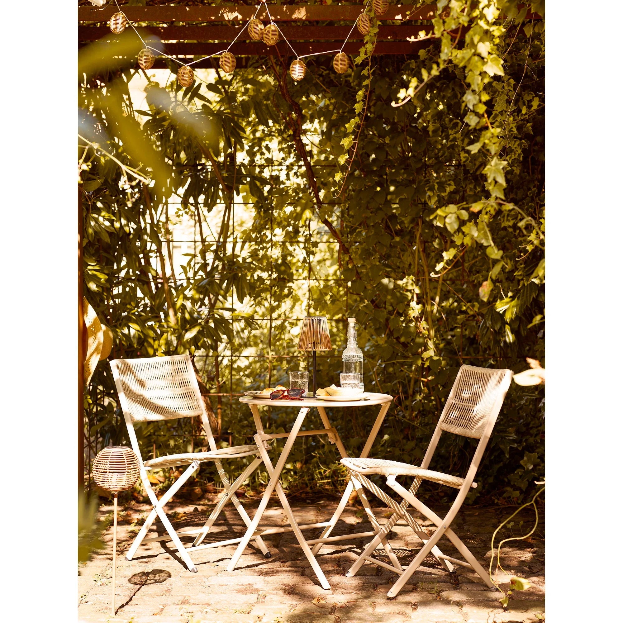 Chaise pliante en rotin blanc avec dossier et assise tissés, sous feuillage vert
