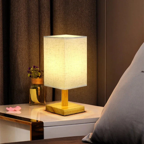 Lampe en bois carré allumée sur une table de chevet