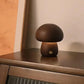 Petite lampe champignon en bois, allumée et posée sur un meuble en bois foncé.