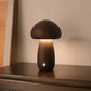 Lampe champignon en bois de taille moyenne allumée sur un meuble, diffusant une lumière douce.