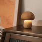Petite lampe champignon en bois foncé allumée, posée sur un meuble, ambiance tamisée.