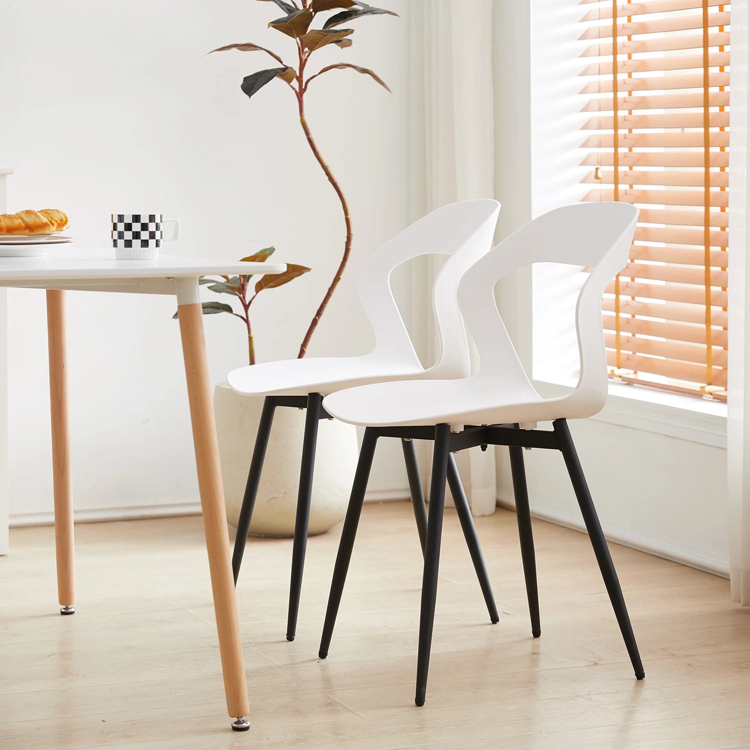 Deux chaises contemporaines blanches avec pieds en métal noir placées près d’une table dans une pièce lumineuse.