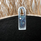 Support en métal fixé à une surface noire texturée avec de la paille au-dessus pour le Miroir rond 75 cm en Raphia et Coquillages Naturel Blanc